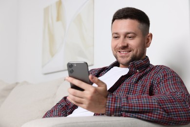 Photo of Man sending message via smartphone on sofa at home
