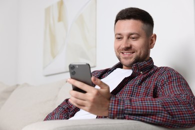 Man sending message via smartphone on sofa at home