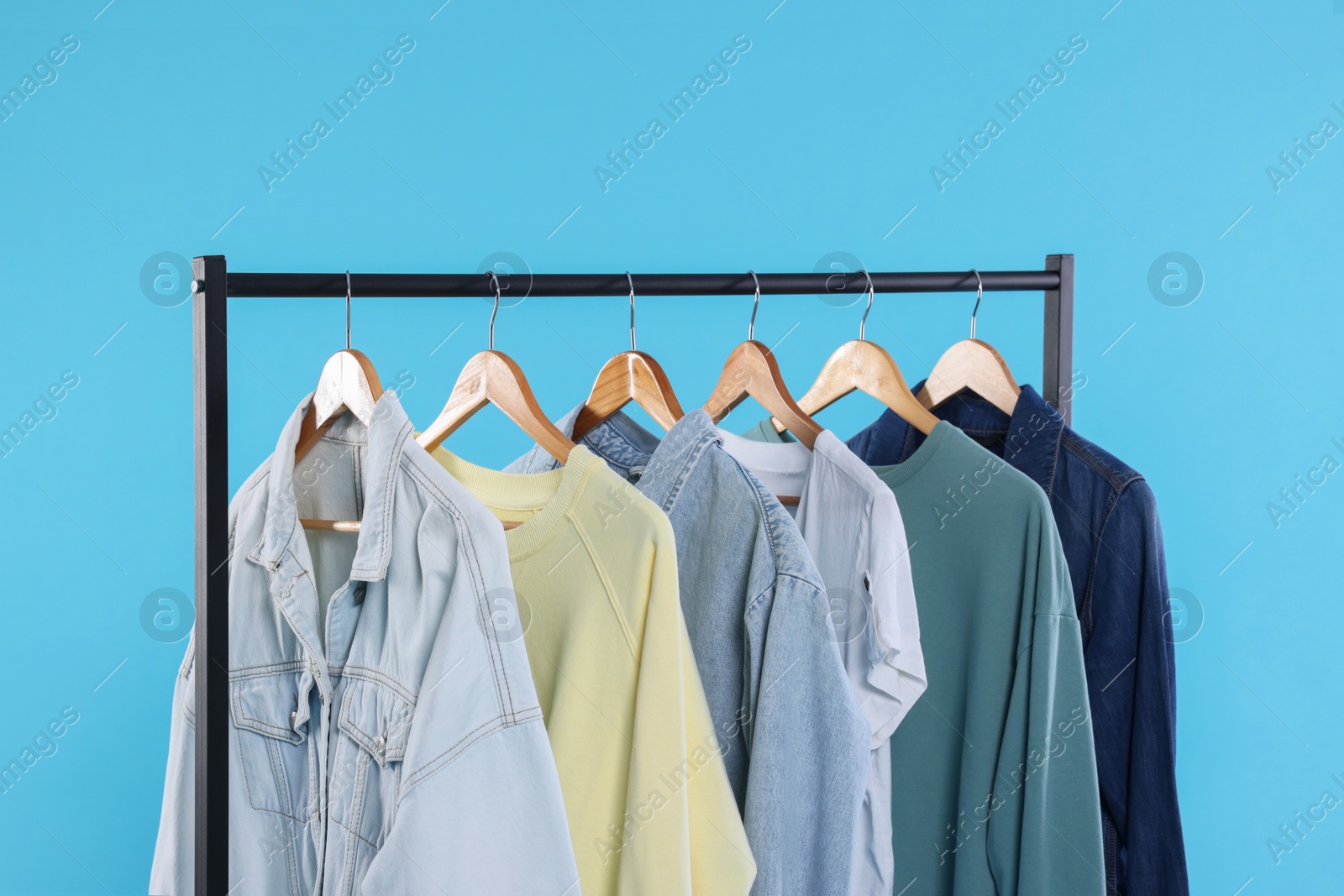 Photo of Rack with stylish clothes on wooden hangers against light blue background