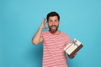 Photo of Emotional man holding gift box on turquoise background