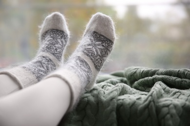 Photo of Woman wearing warm socks on knitted plaid near window, closeup. Space for text