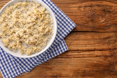 Tasty boiled oatmeal in bowl on wooden table, top view. Space for text