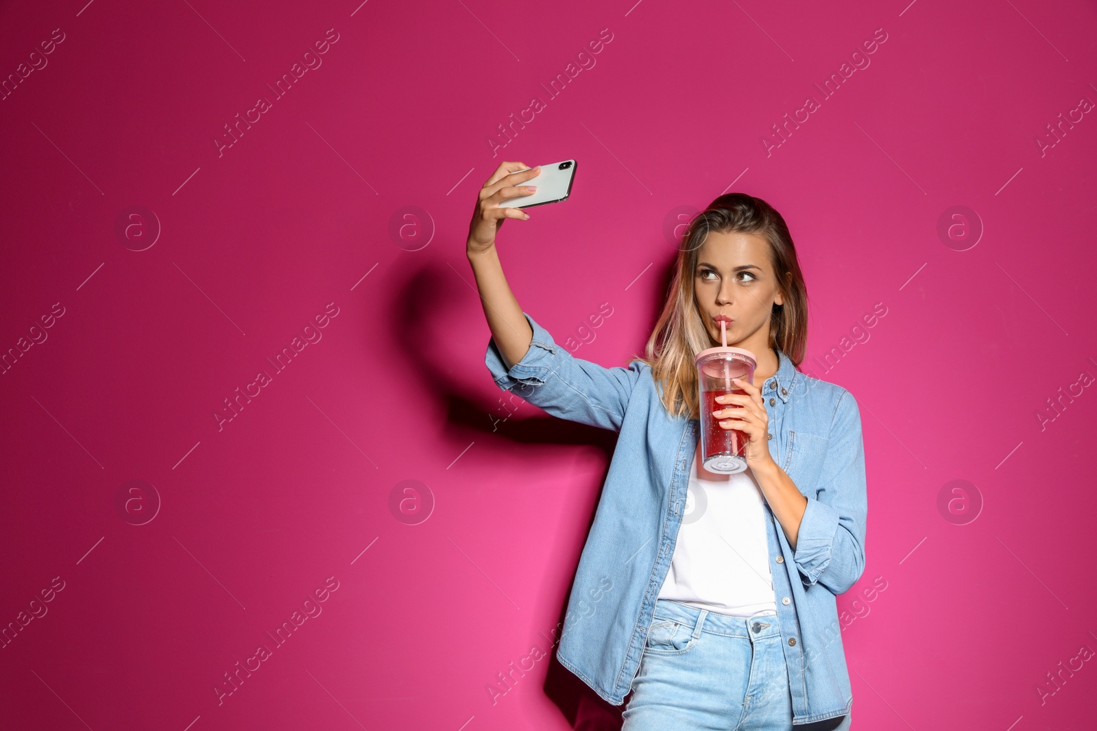 Photo of Beautiful woman with tasty drink taking selfie on color background