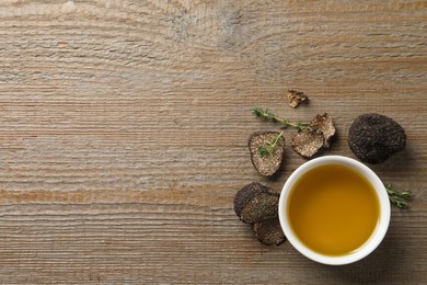 Photo of Fresh truffles and oil in bowl on wooden table, flat lay. Space for text