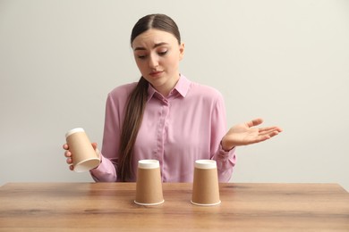 Photo of Disappointed woman playing shell game at wooden table