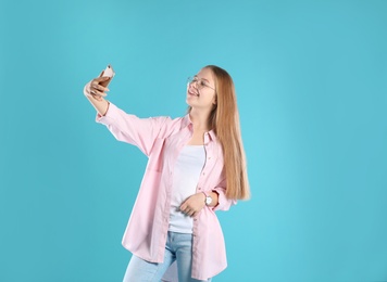 Pretty teenage girl taking selfie on color background