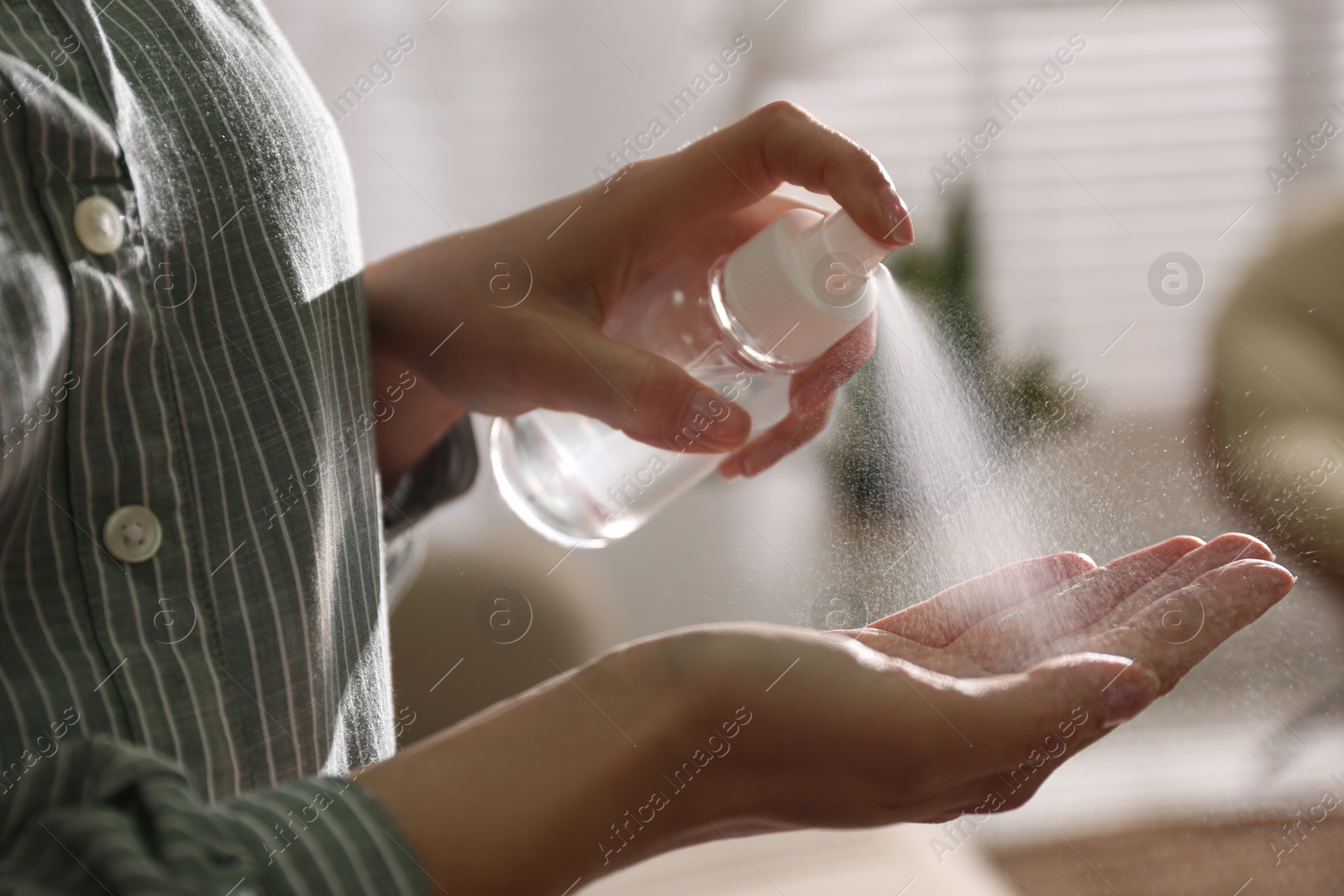 Photo of Woman spraying antiseptic onto hand indoors, closeup