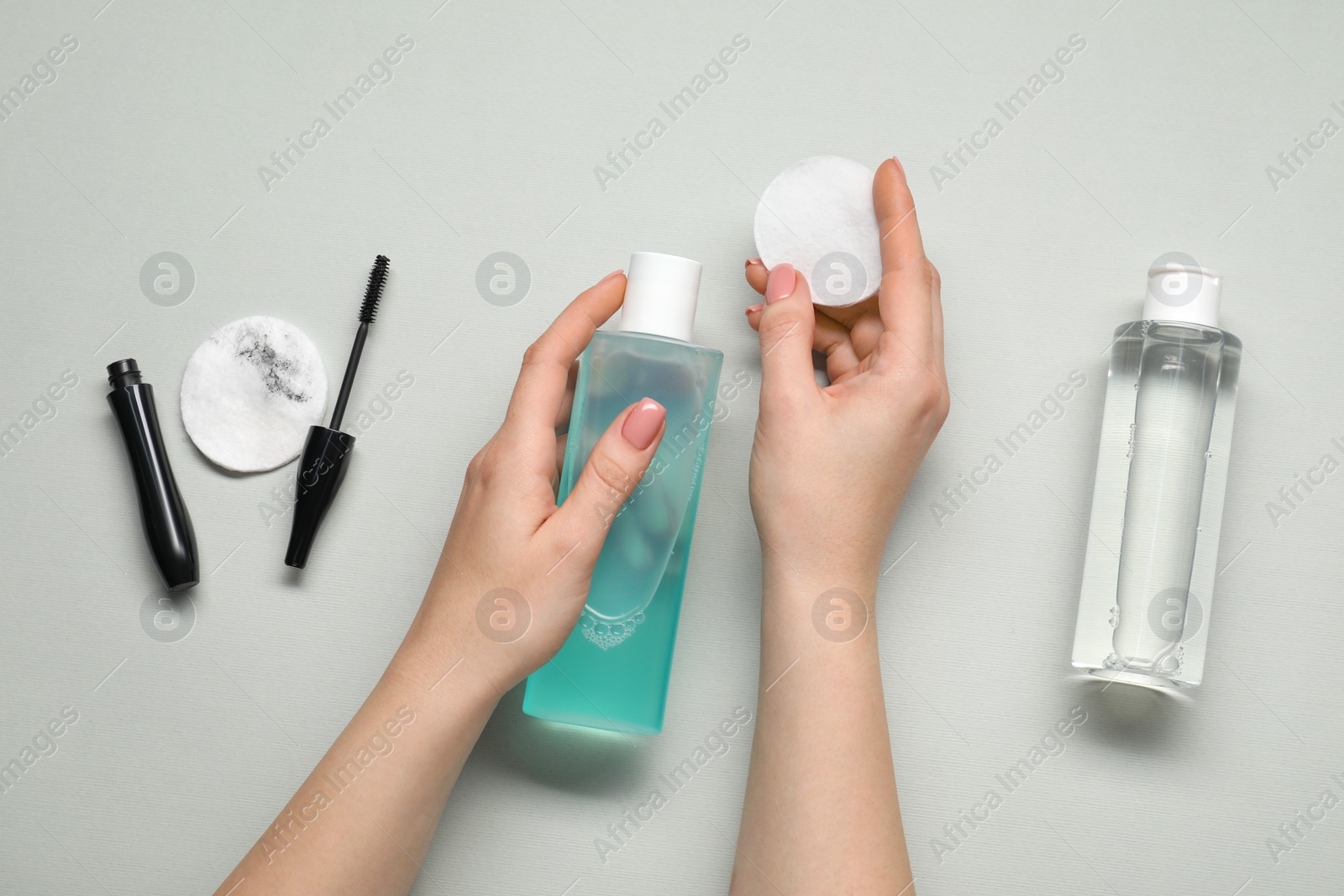 Photo of Woman with makeup remover, cotton pads, cosmetic product and mascara on light grey background, top view