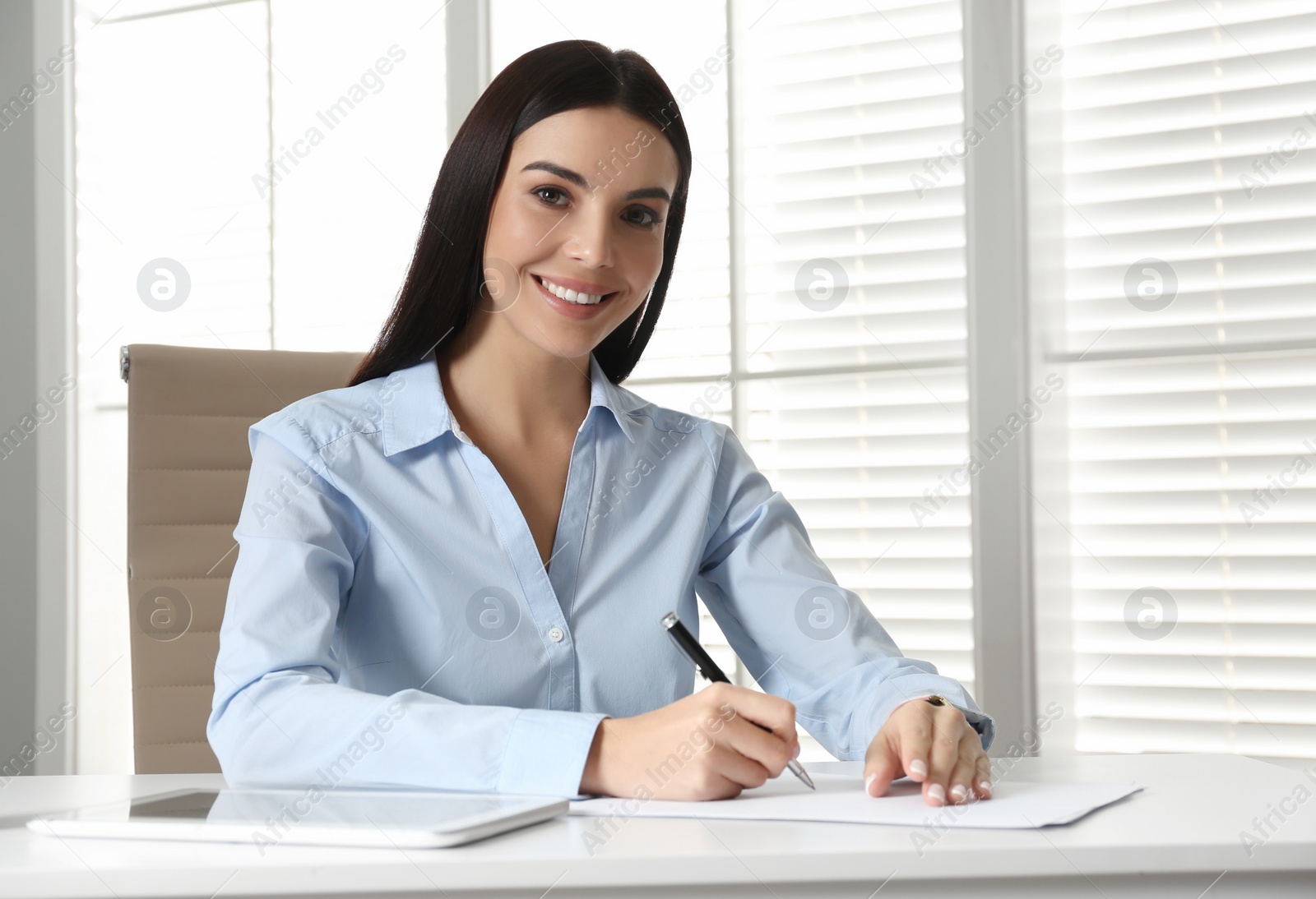 Photo of Young businesswoman writing at table in office