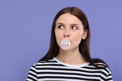 Photo of Beautiful woman blowing bubble gum on light purple background, space for text