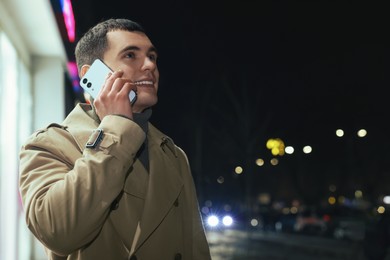 Man talking by smartphone on night city street, space for text