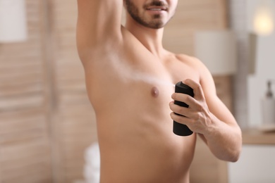 Handsome young man applying deodorant in bathroom