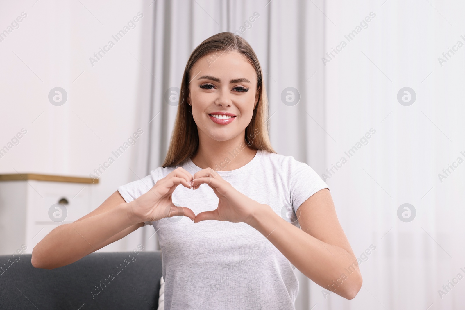 Photo of Happy woman showing heart gesture with hands at home