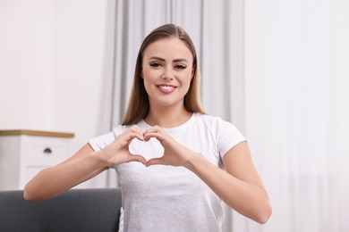 Happy woman showing heart gesture with hands at home