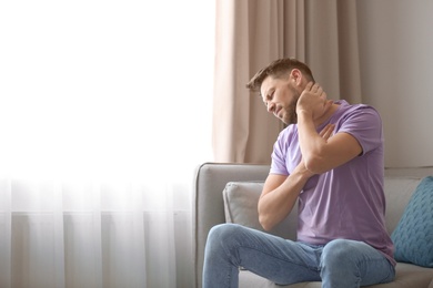 Photo of Young man suffering from neck pain at home