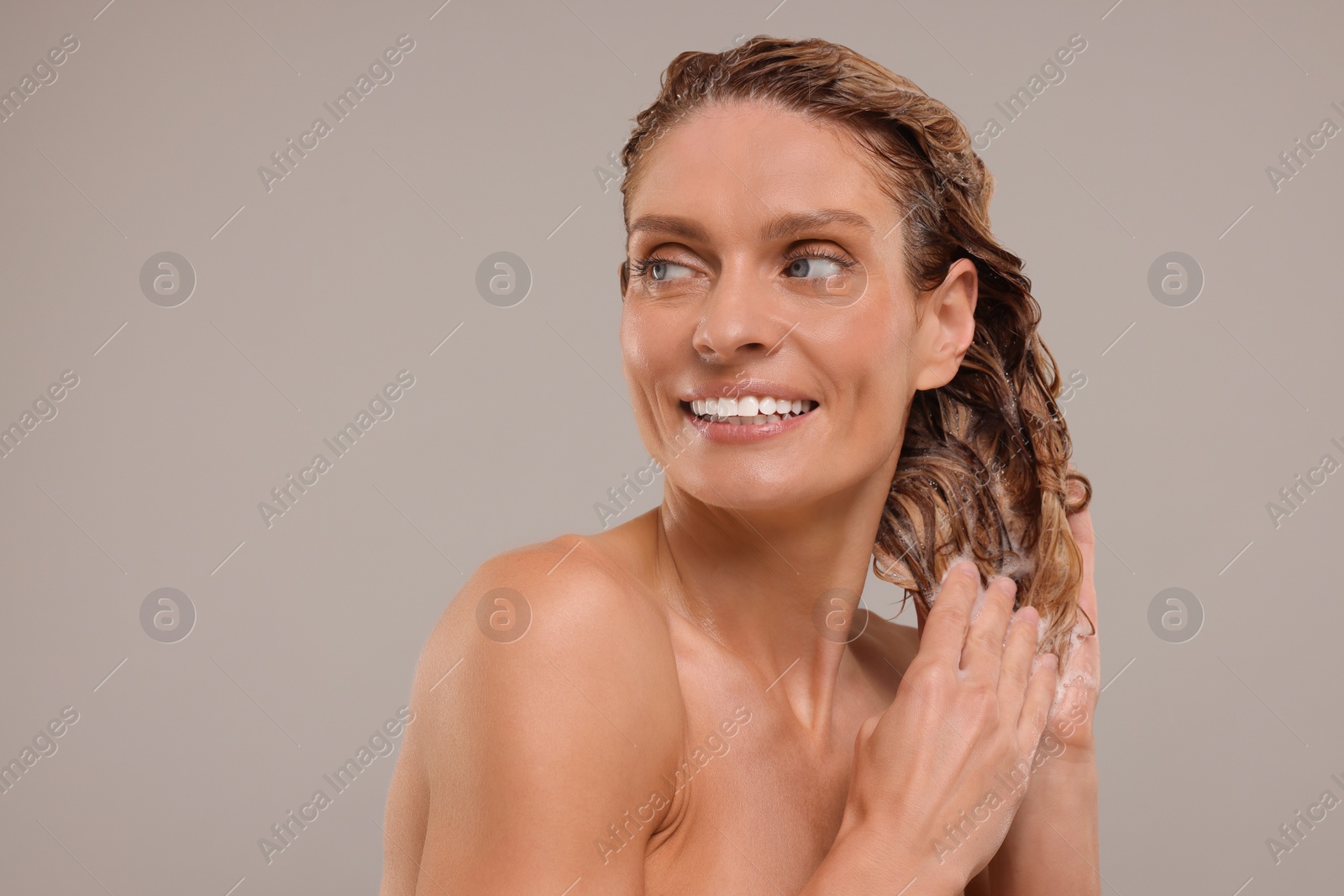 Photo of Portrait of beautiful happy woman washing hair on light grey background