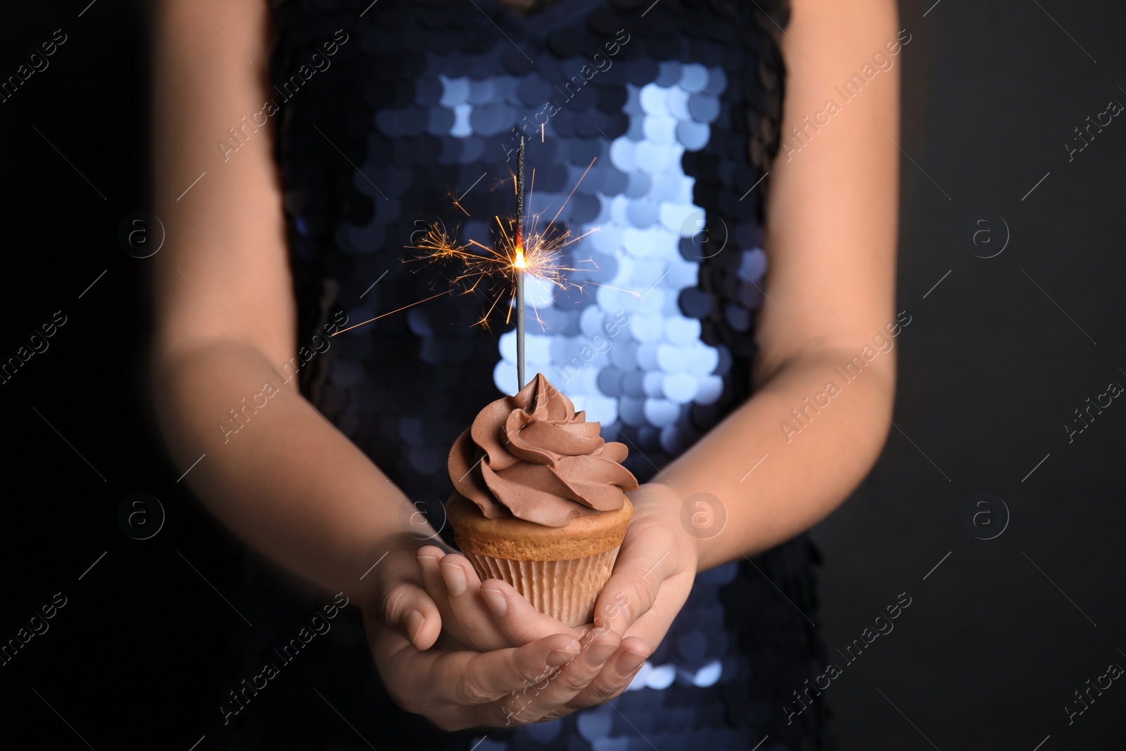 Photo of Woman holding birthday cupcake with sparkler on black background, closeup