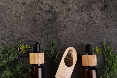 Photo of Bottles of essential oil and scoop with fresh dill on grey table, flat lay. Space for text