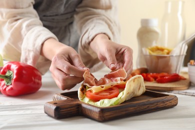 Photo of Woman cooking delicious pita wrap with jamon, cheese and vegetables at wooden table, closeup