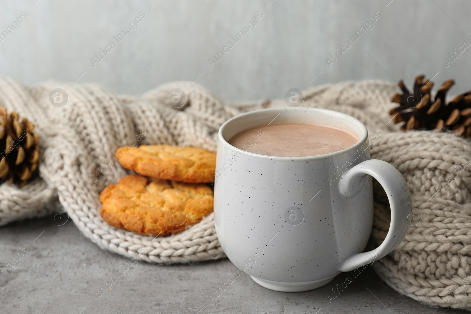 Photo of Delicious hot cocoa drink in cup, cookies and knitted blanket on grey surface