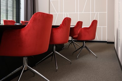 Photo of Stylish red office chairs and large table in empty conference room