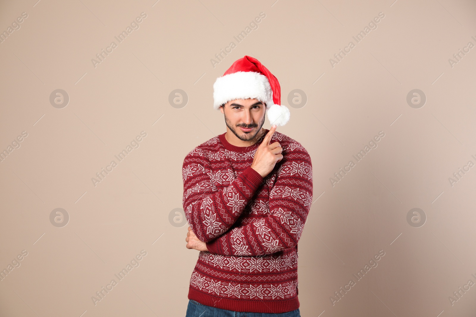 Photo of Portrait of young man in Christmas sweater and Santa hat on beige background