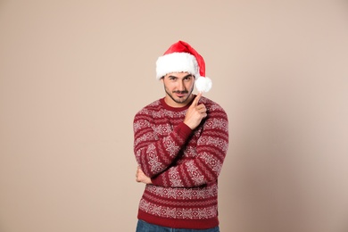 Photo of Portrait of young man in Christmas sweater and Santa hat on beige background