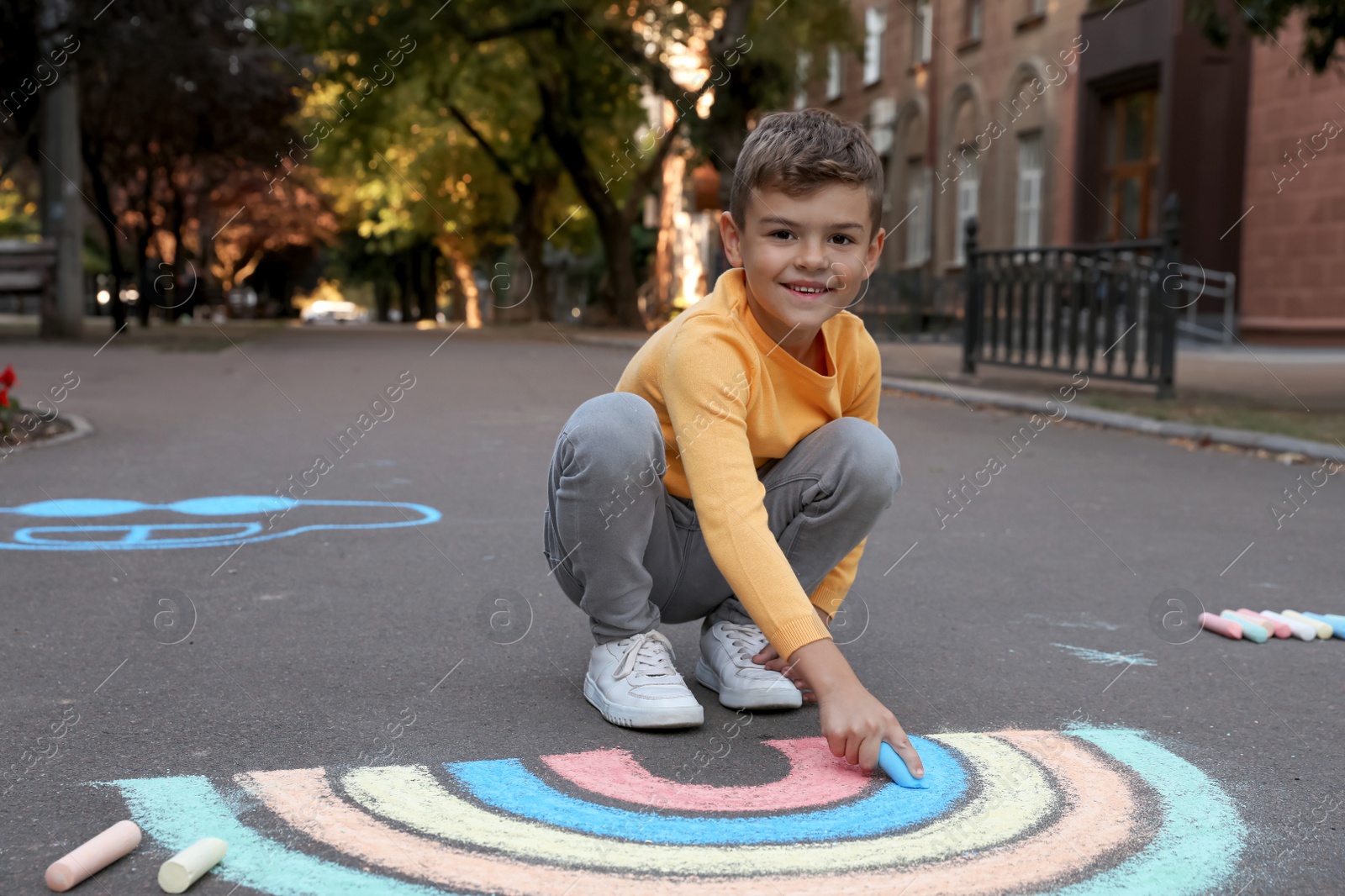 Photo of Happy child drawing rainbow with chalk on asphalt