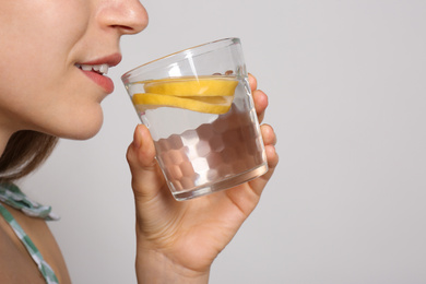 Photo of Young woman drinking lemon water on light background, closeup