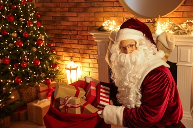 Photo of Santa Claus with sack of gifts in festively decorated room