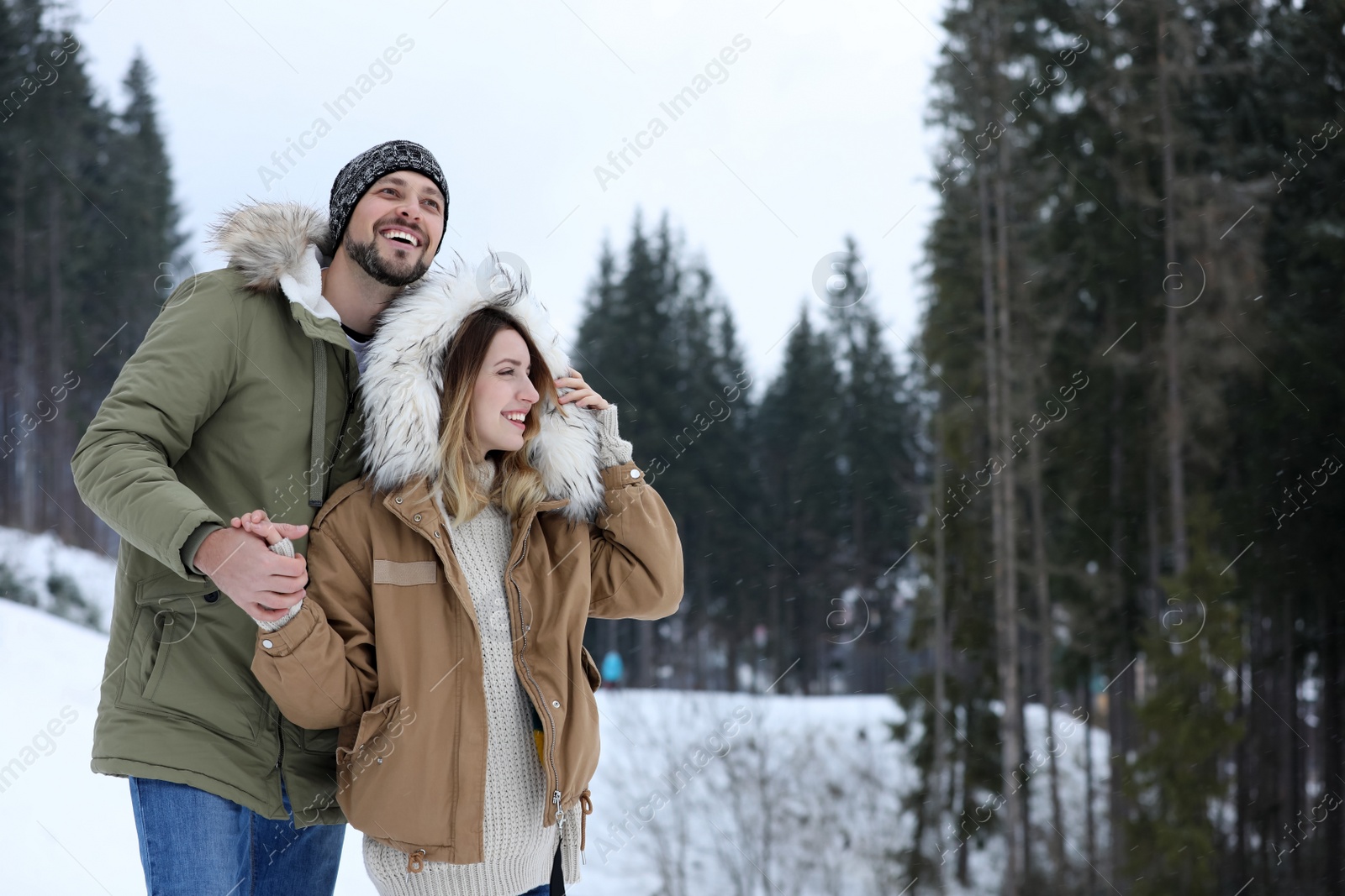 Photo of Happy couple near conifer forest on snowy day, space for text. Winter vacation