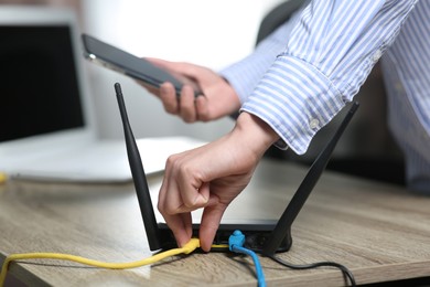Photo of Woman with smartphone connecting cable to Wi-Fi router at wooden table indoors, closeup