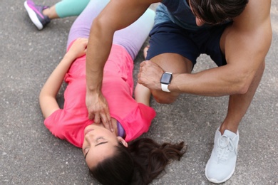 Photo of Young man checking pulse of unconscious woman on street