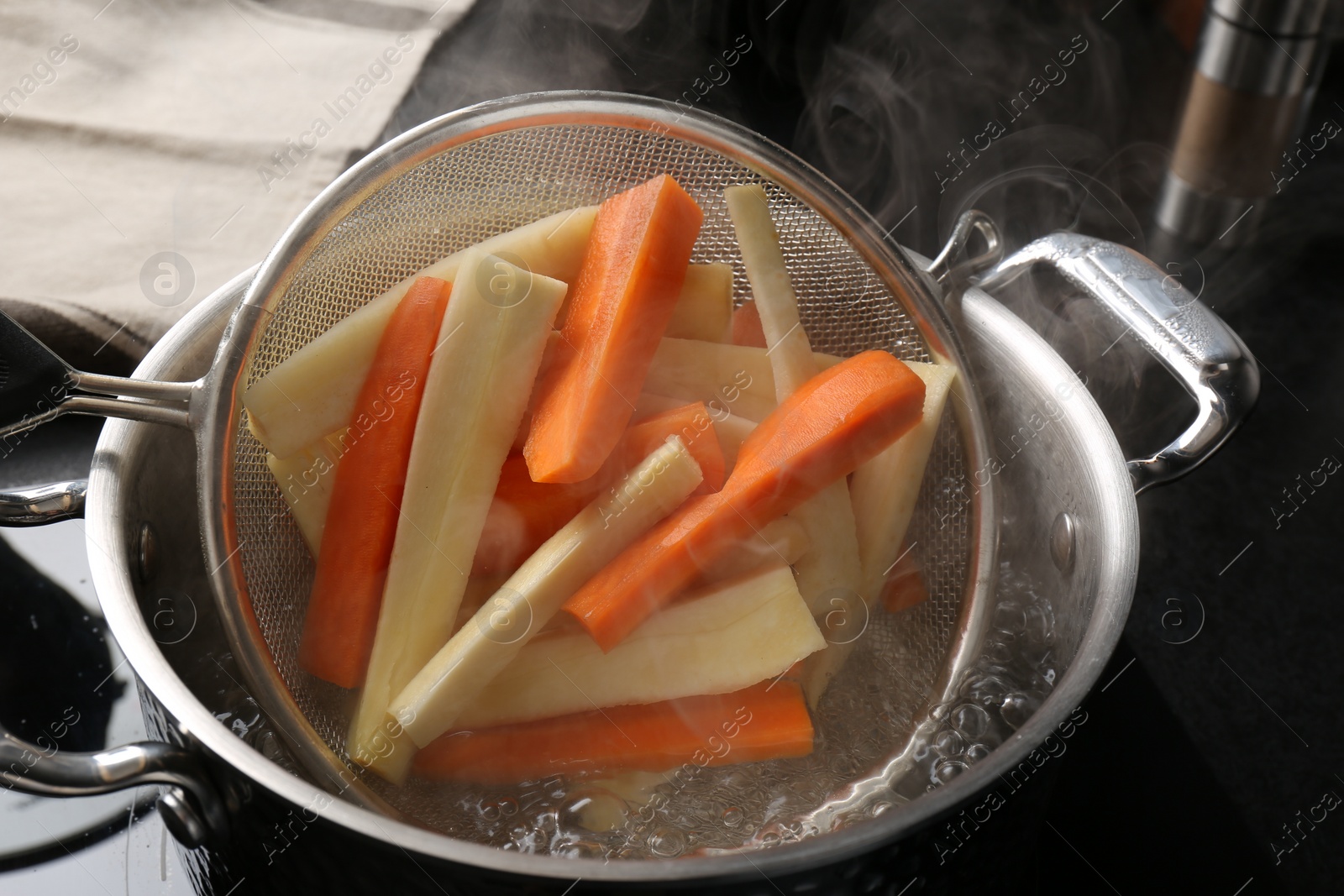 Photo of Putting cut parsnips and carrots into pot with boiling water in kitchen, closeup