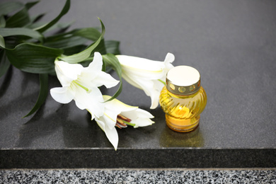 Photo of White lilies and candle on black granite tombstone. Funeral ceremony