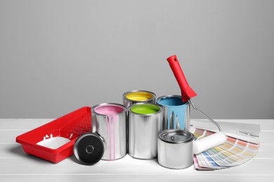 Cans of paints, roller, tray and palette on white wooden table