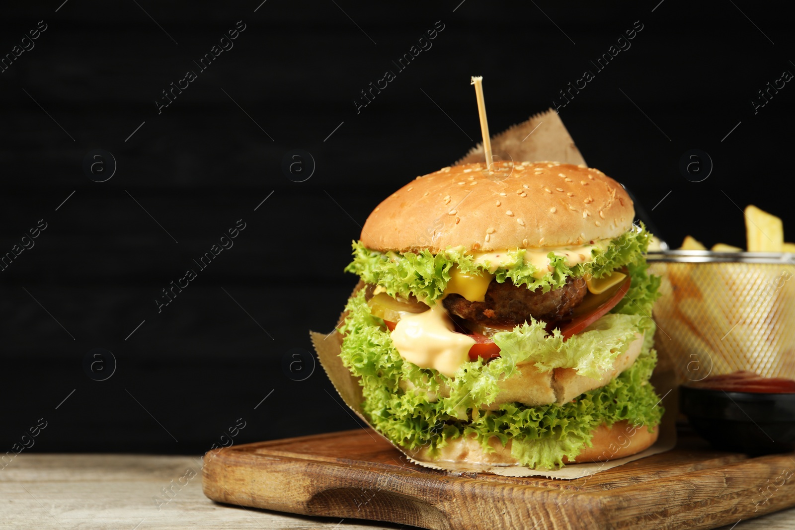 Burger with delicious patty, french fries and sauce on wooden table against dark background, space for text Photo of Burger with delicious patty, french fries and sauce on wooden table against dark background, space for text