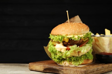 Photo of Burger with delicious patty, french fries and sauce on wooden table against dark background, space for text