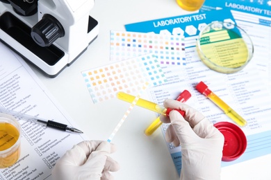 Photo of Doctor holding test tube with urine sample for analysis at white table, top view