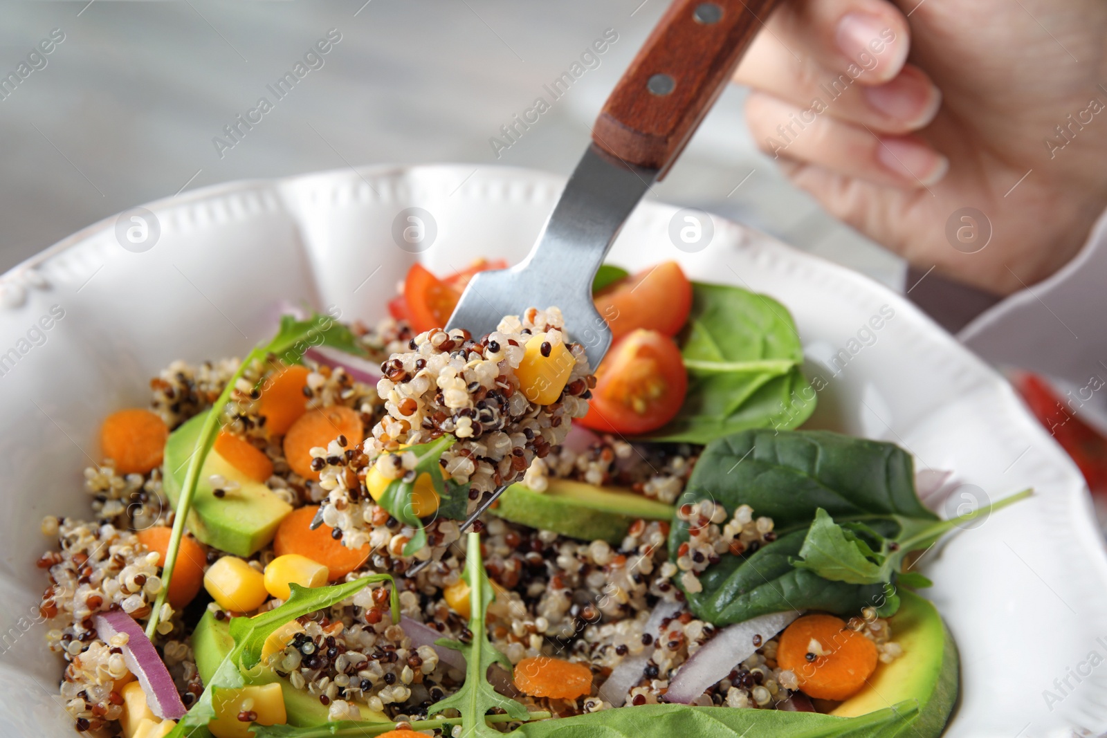 Photo of Woman eating healthy quinoa salad with vegetables from plate, closeup