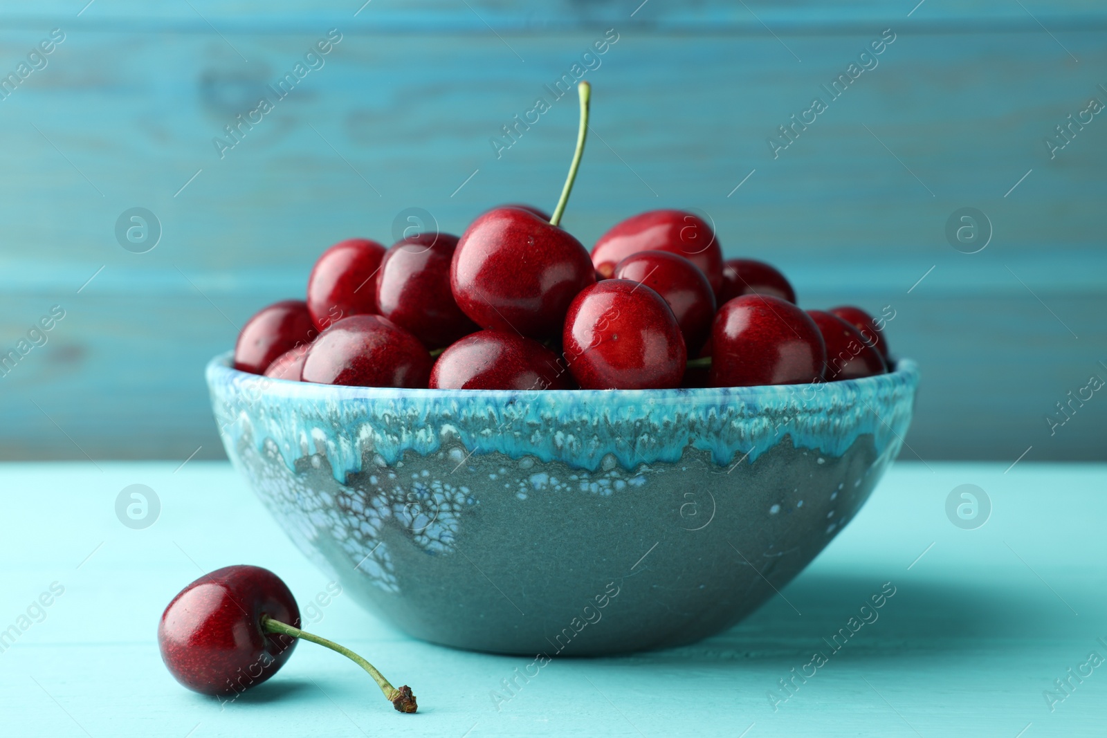 Photo of Fresh ripe cherries in bowl on turquoise wooden table, closeup