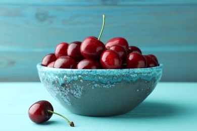 Photo of Fresh ripe cherries in bowl on turquoise wooden table, closeup