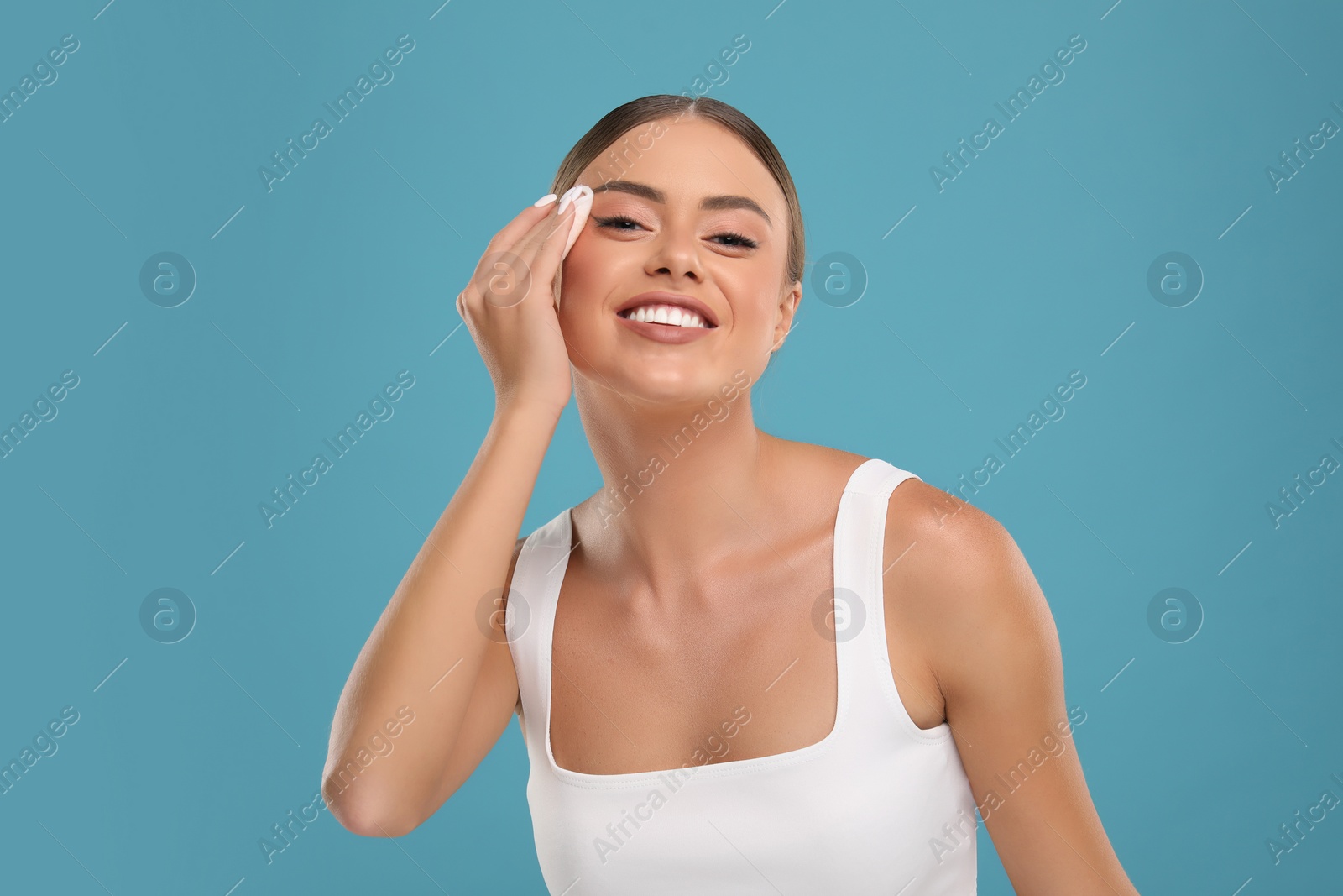 Photo of Beautiful woman removing makeup with cotton pad on light blue background