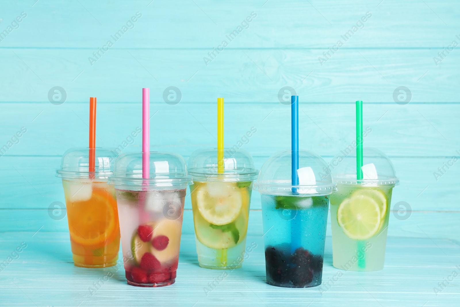 Photo of Plastic cups with lemonades on table against color background