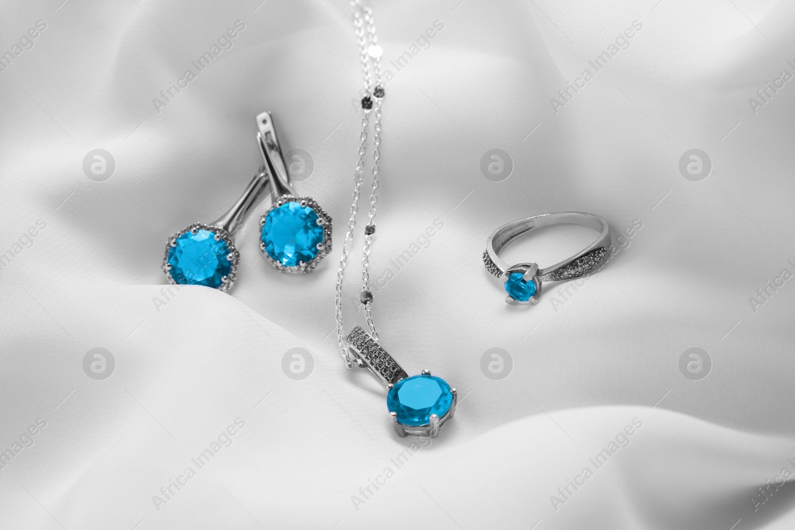 Photo of Beautiful jewelry with light blue gemstones on white fabric