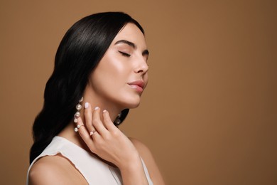 Young woman wearing elegant pearl jewelry on brown background, space for text