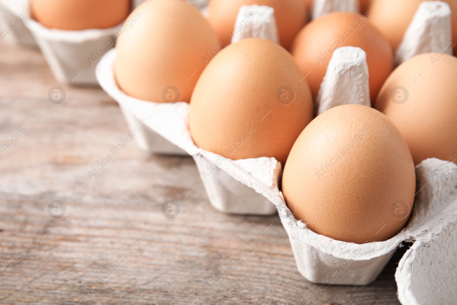 Photo of Carton of eggs on wooden table, closeup view