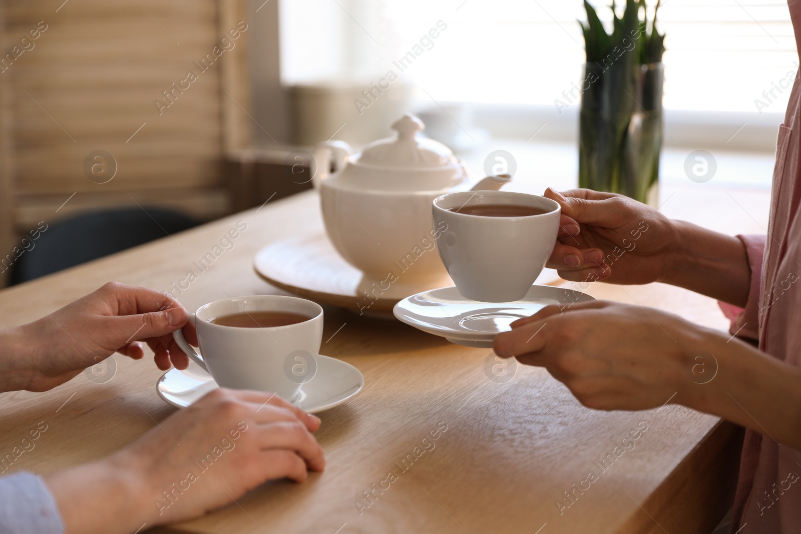 Photo of Women with cups of tea at table near window indoors, closeup