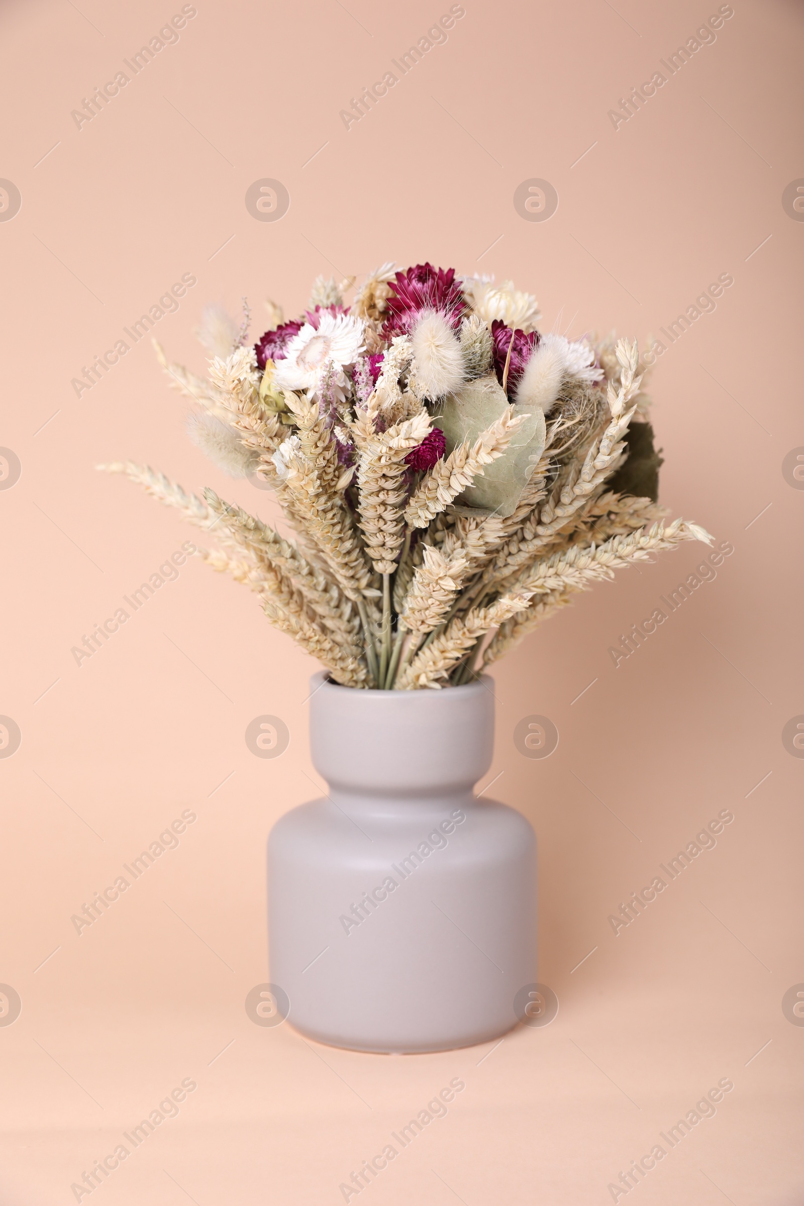 Photo of Bouquet of beautiful dry flowers and spikelets in vase on beige background