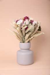 Bouquet of beautiful dry flowers and spikelets in vase on beige background